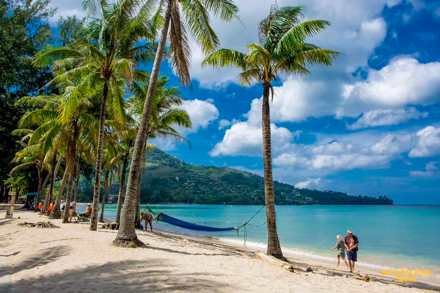People stroll and relax on a beautiful sandy beach with palm trees and clear water in Phuket.