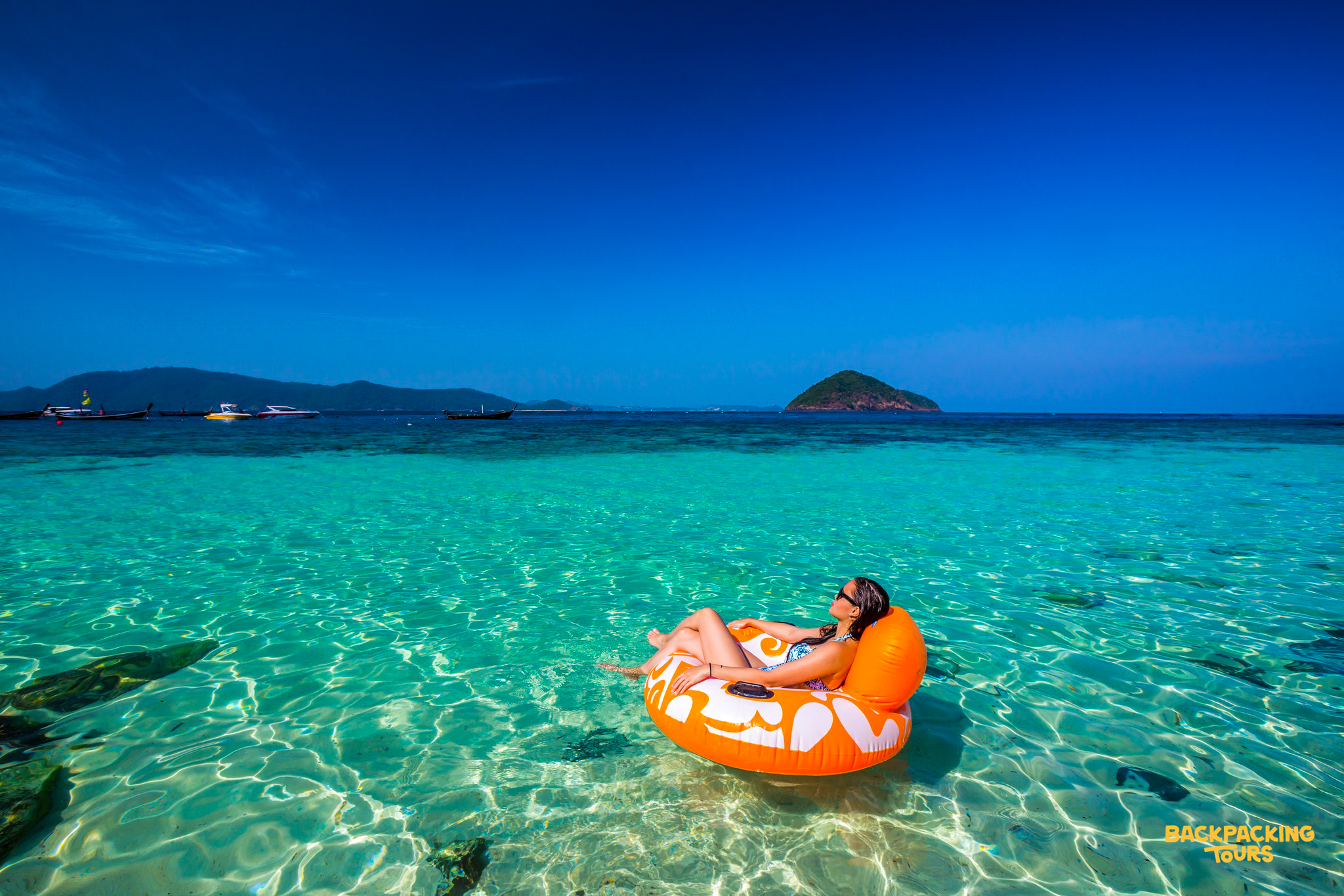 A woman relaxes on an orange float in the clear turquoise waters of Phuket, enjoying a sunny day.