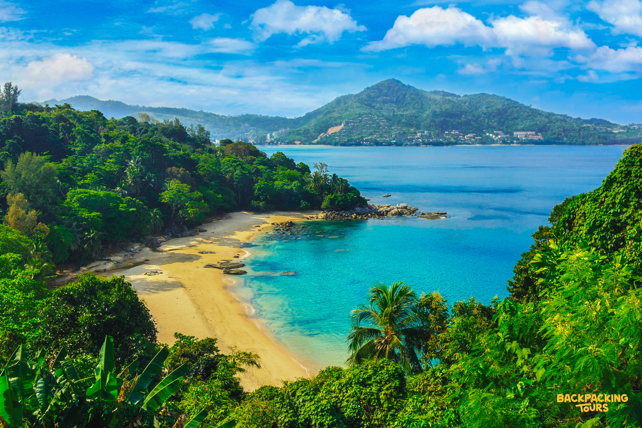 Beautiful tropical beach in Phuket, featuring clear turquoise water, golden sand, and vibrant green hills.