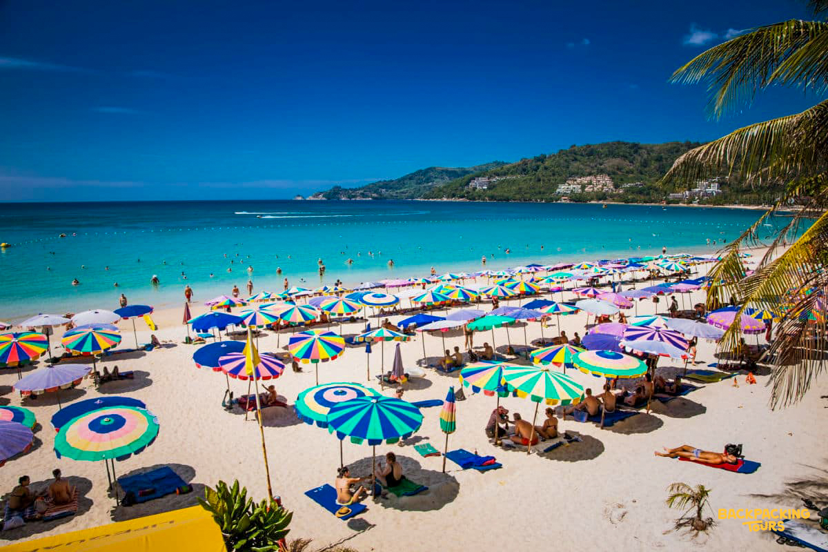 Vibrant beach scene in Phuket with colorful umbrellas, sunbathers, and people enjoying the clear turquoise water.
