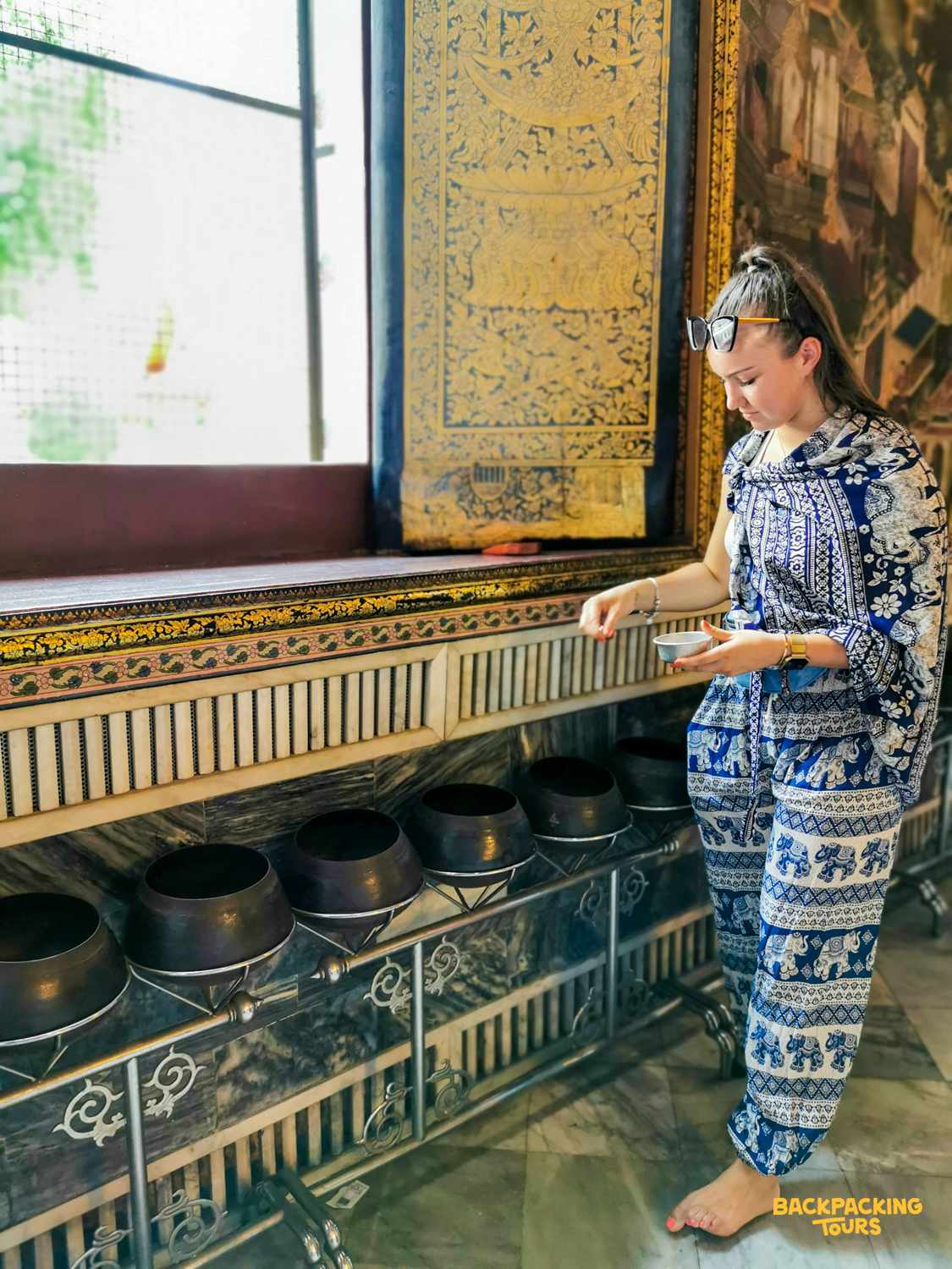 A woman makes a traditional offering into a row of bowls at a beautiful temple in Bangkok.