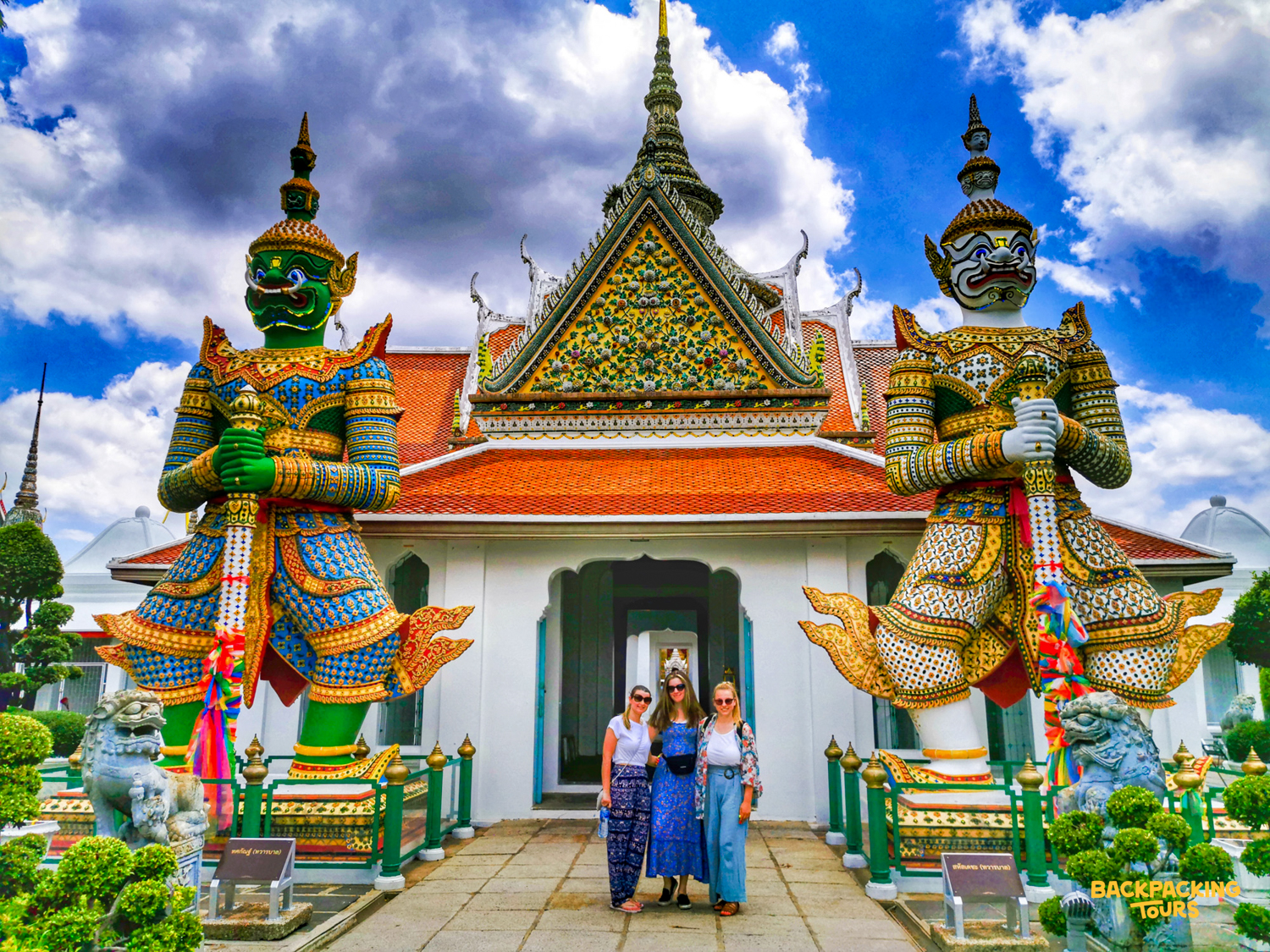Three friends pose in front of a vibrant Thai temple with giant guardian statues in Bangkok.
