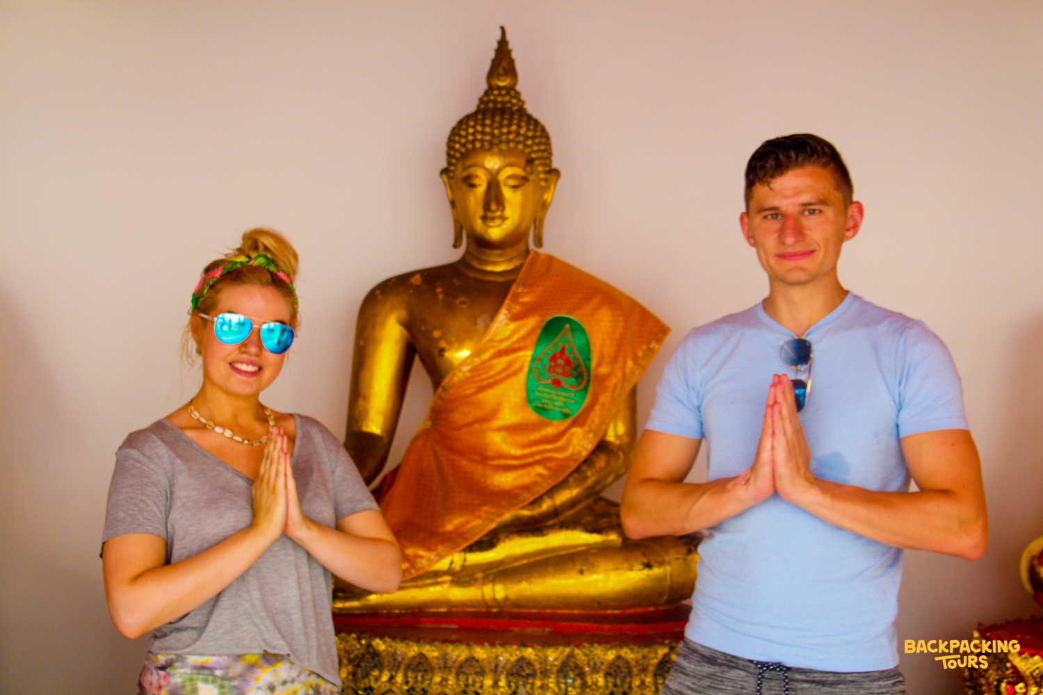 Two travelers respectfully pose with a golden Buddha statue in a temple in Bangkok.