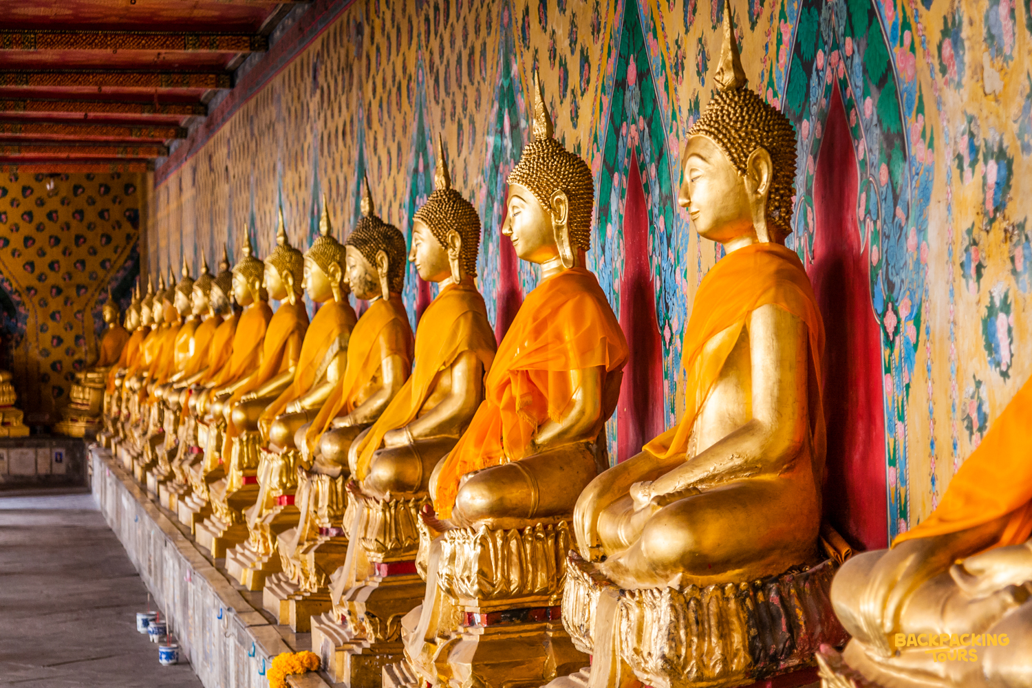 Rows of golden Buddha statues in orange robes create a peaceful scene within a Bangkok temple.