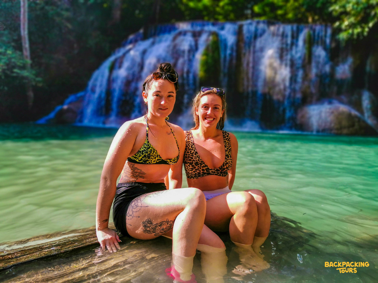 Two happy women relaxing in the emerald pools of Erawan Waterfalls in Thailand.