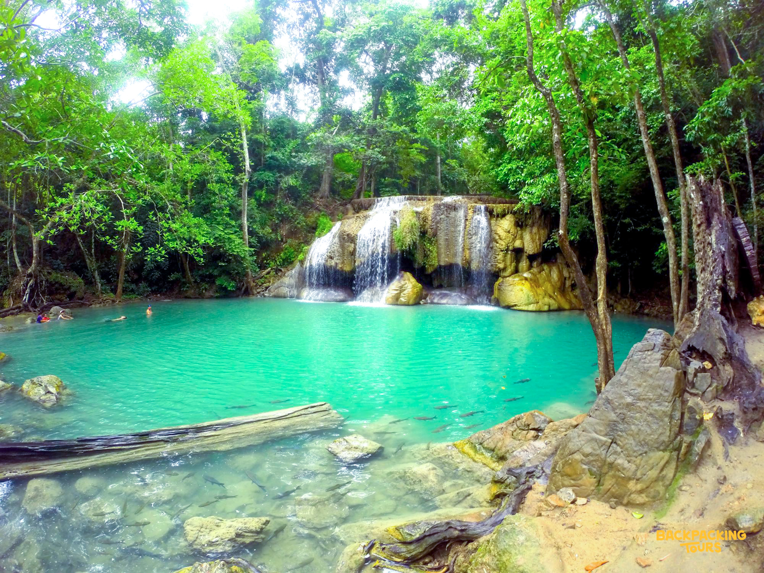 Swimmers enjoy the emerald green pools of Erawan Waterfalls surrounded by lush jungle.