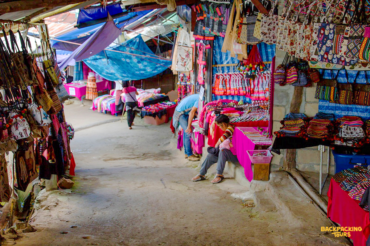Visitors browse vibrant handmade textiles and crafts at a bustling market in a Hmong village, Chiang Mai.
