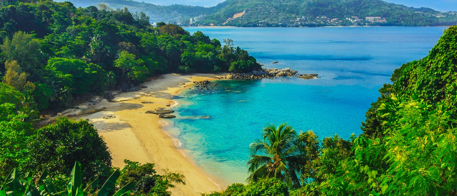 Beautiful Phuket beach from above, featuring clear turquoise water, golden sand, and dense green jungle.