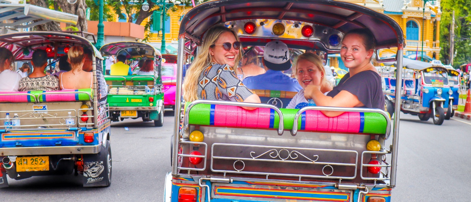 Smiling friends enjoy a lively tuk-tuk ride through the vibrant city streets of Bangkok.