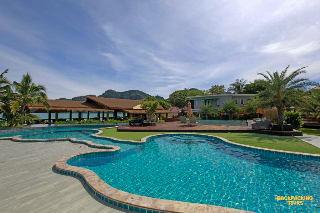 Spacious resort accommodation featuring multiple swimming pools, palm trees, and island mountains on Phi Phi Islands.