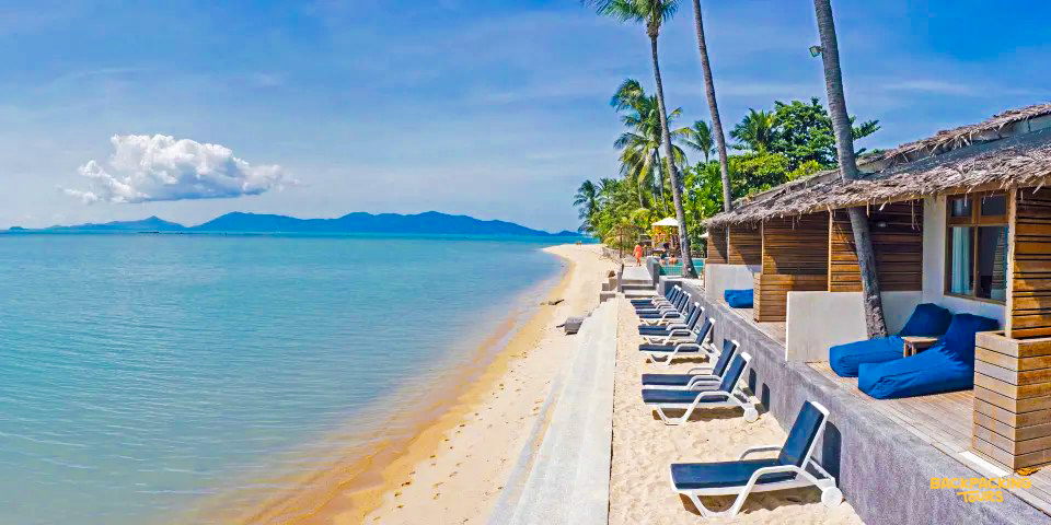Charming beach resort on Koh Samui with bungalows, sun loungers, and palm trees by the turquoise sea.