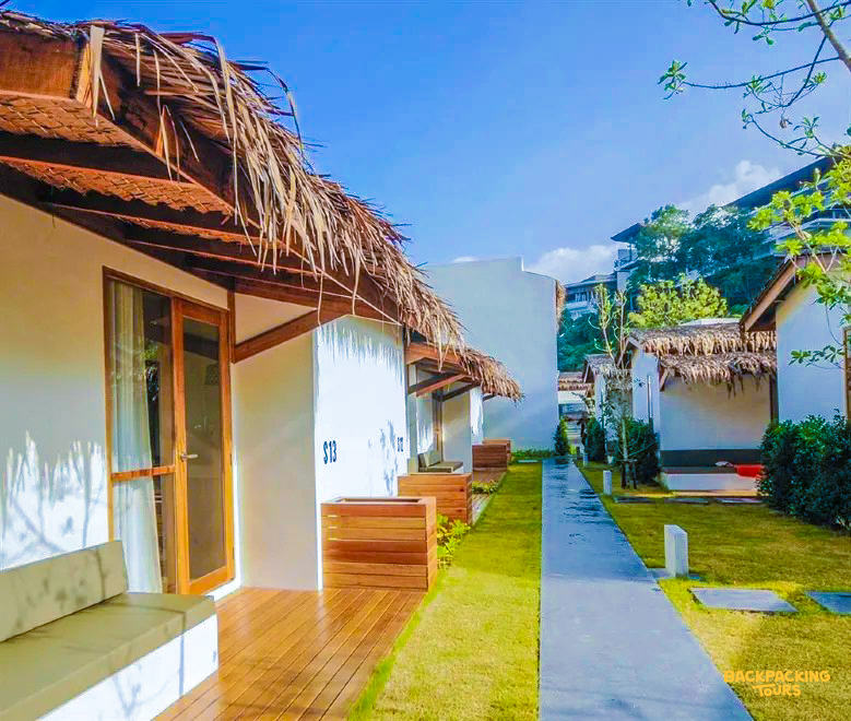 A serene pathway between white bungalows with thatched roofs at a tropical resort in Koh Samui.