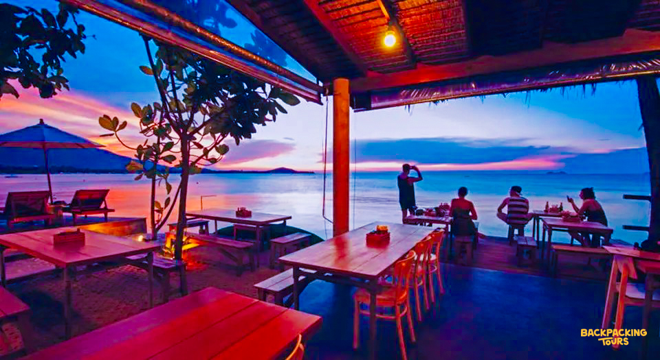 People enjoy a vibrant sunset from an open-air restaurant overlooking the calm sea in Koh Samui.