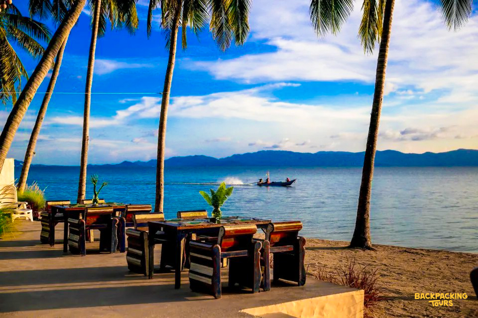 Relaxing tropical beach restaurant with palm trees, overlooking the calm blue sea and distant land.