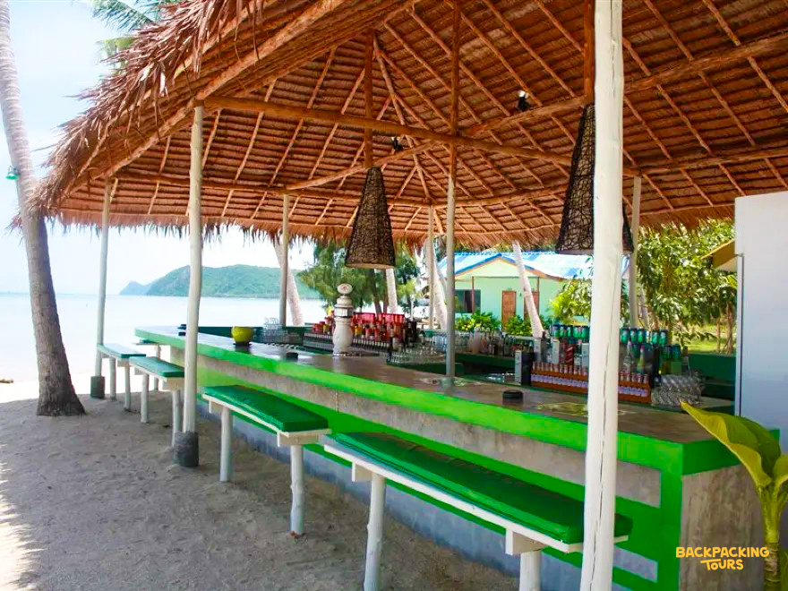 A tropical beach bar with a thatched roof and green benches on Koh Phangan.
