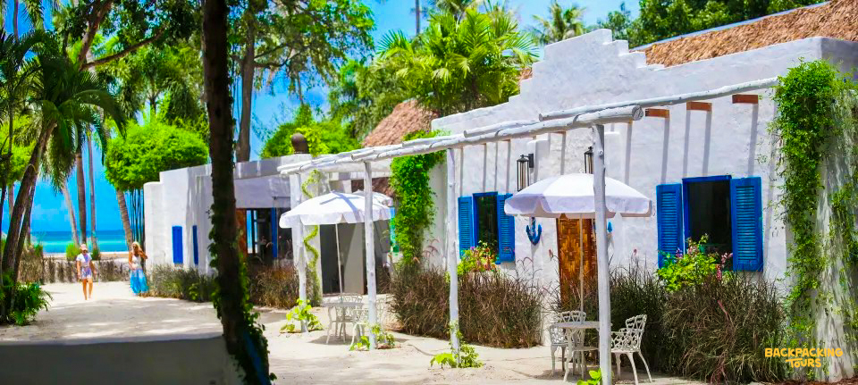 Guests walk past white bungalows with blue shutters towards the beautiful beach on Koh Phangan.