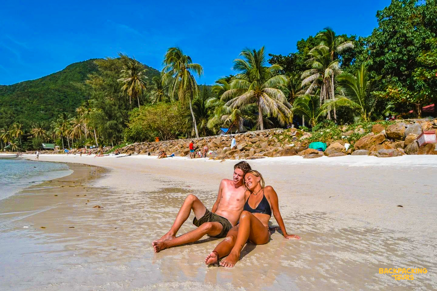 A happy couple relaxes on a sunny sandy beach in Koh Samui with palm trees.
