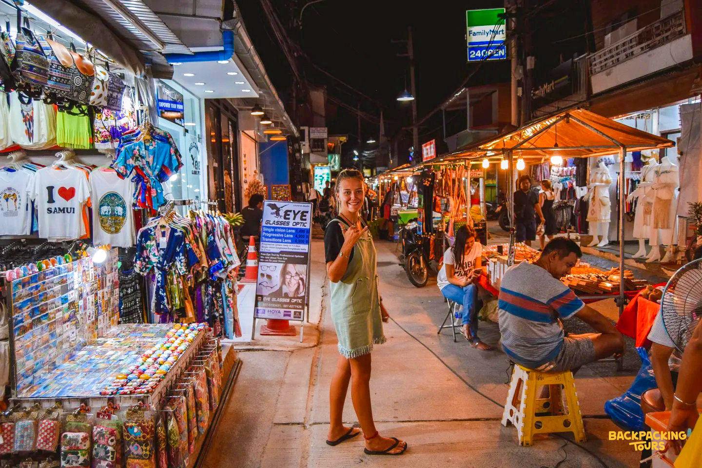 Smiling woman gives a thumbs-up at a bustling night market in Fisherman's Village, Koh Samui.