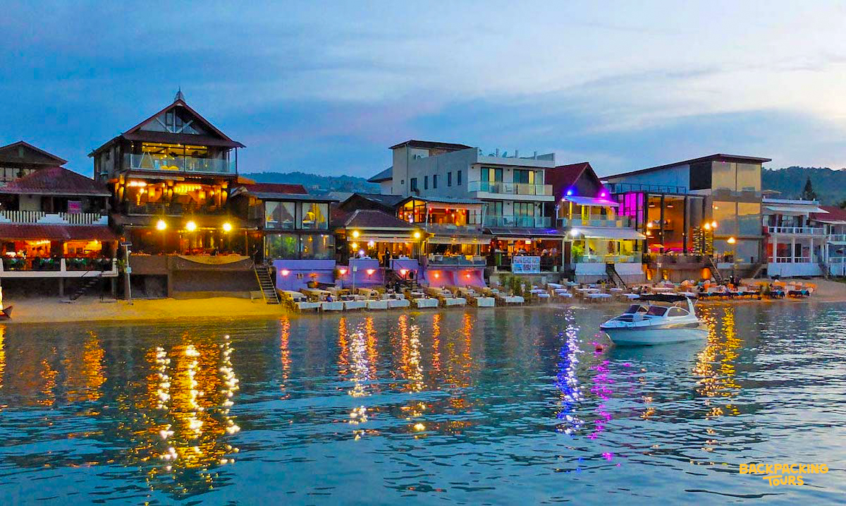 Lively evening scene at Fisherman's Village, Koh Samui, with colorful lights reflecting on the calm water.