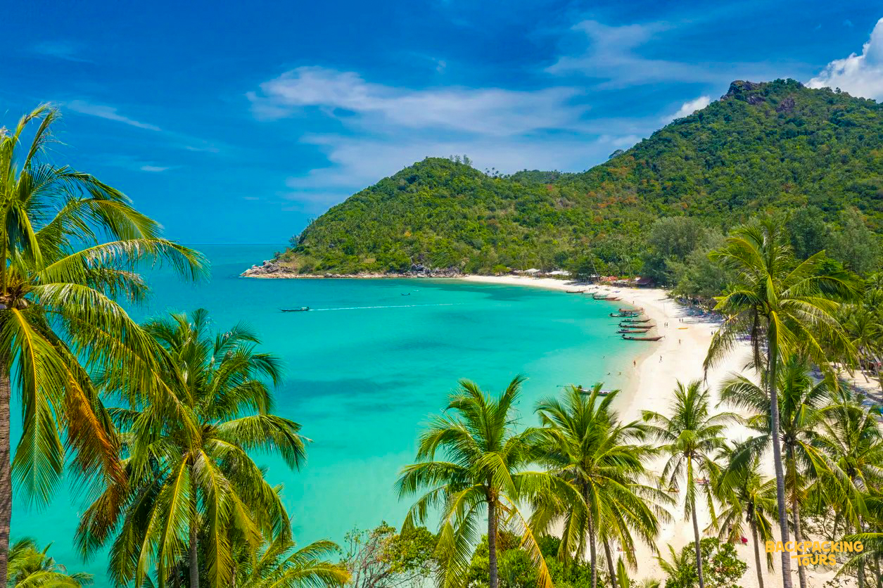 Pristine white sand beach, clear turquoise water, and lush green hills on Koh Phangan.