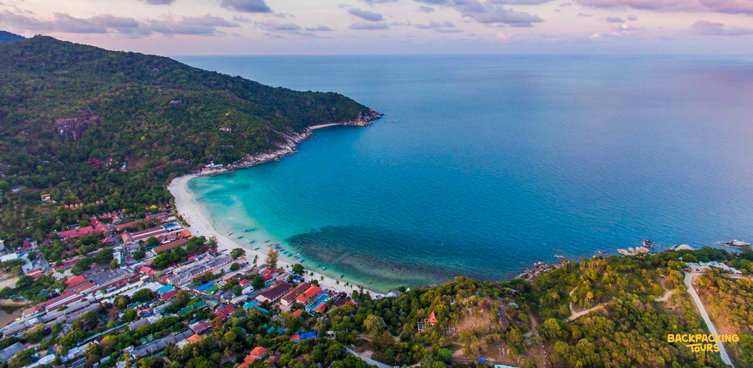 Relaxing tropical bay on Koh Phangan with turquoise water, white sand, and lush green hills.