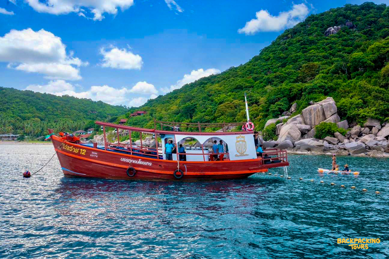 A traditional red longtail boat anchored in turquoise waters near lush green islands in Thailand.