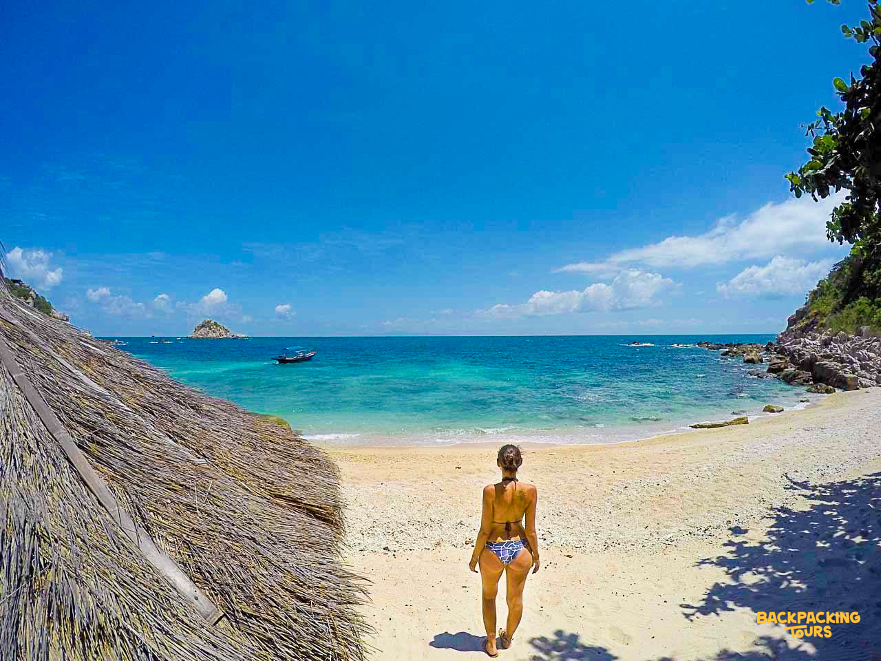 A woman in a bikini walks towards the clear blue ocean on a sandy beach in Koh Tao.