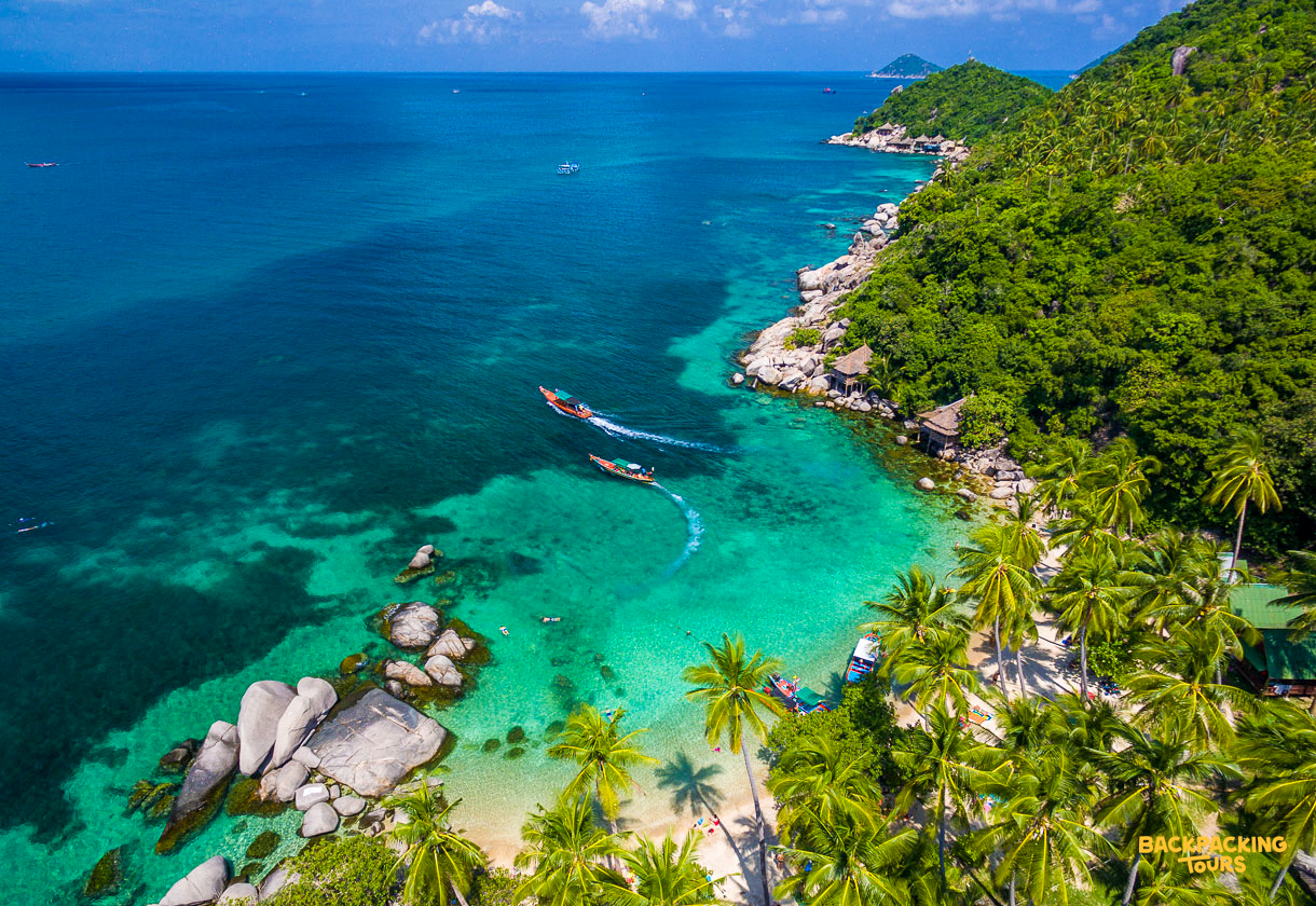 Longtail boats navigate the vibrant turquoise waters of Koh Tao, passing sandy beaches and lush green hills.