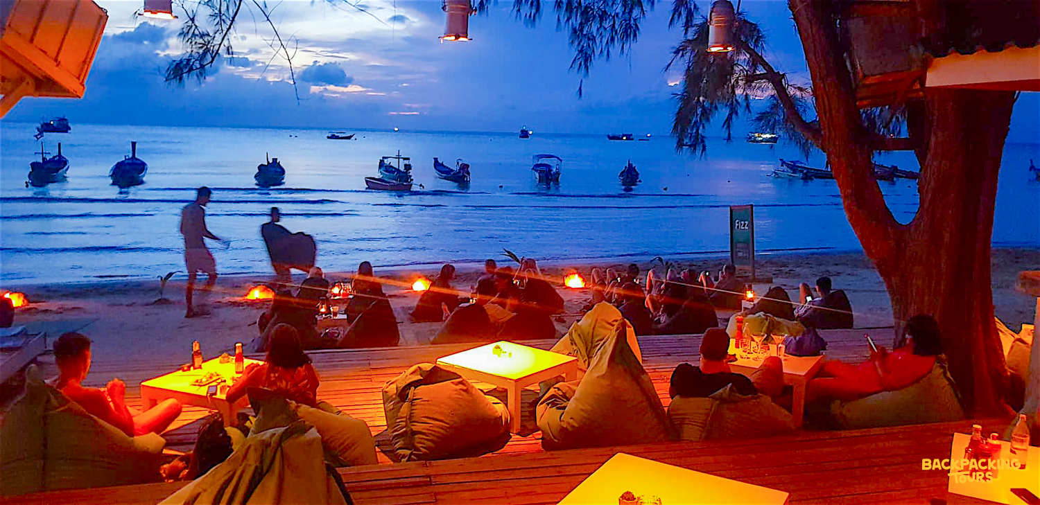Travelers relax on bean bags at a cozy beach bar on Koh Tao as dusk settles.
