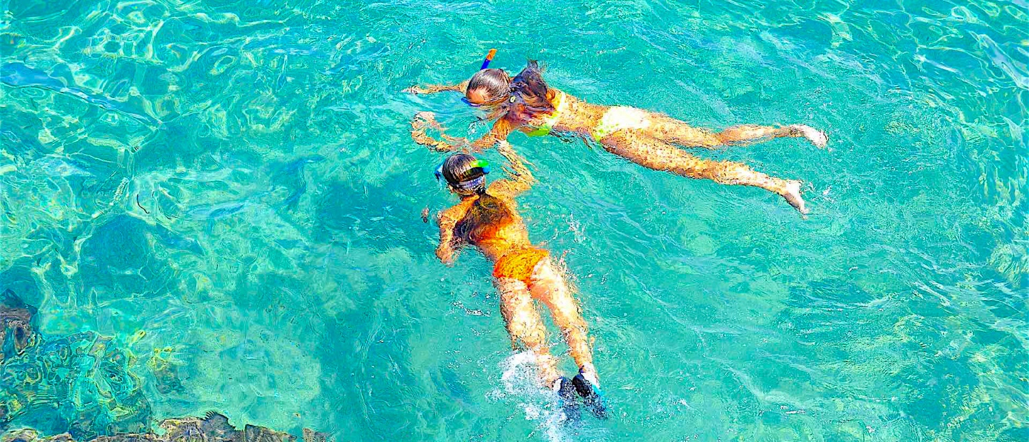 Two women snorkel in the crystal clear turquoise waters of Koh Tao, Thailand.