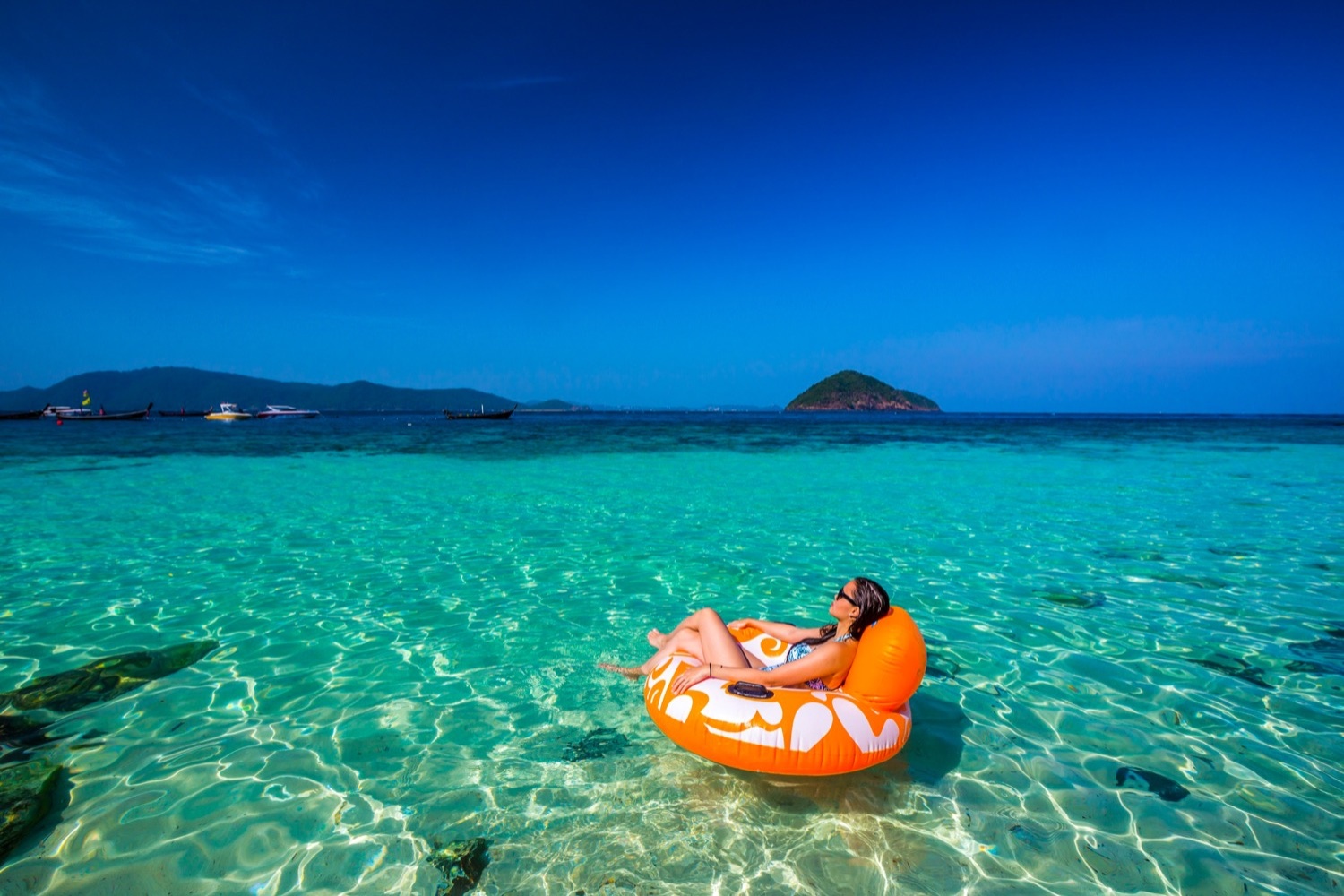 Woman relaxing on an orange float in crystal clear turquoise water off a Thai island.