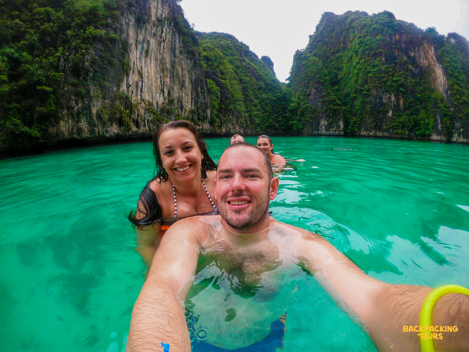 A happy couple takes a selfie while swimming in the clear turquoise waters of Phi Phi Islands.