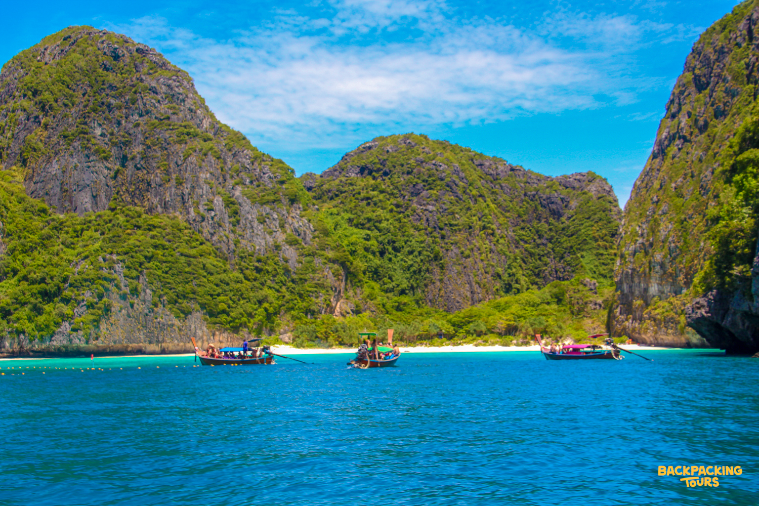 Longtail boats in the turquoise waters of a beautiful bay surrounded by lush cliffs, Phi Phi Islands.