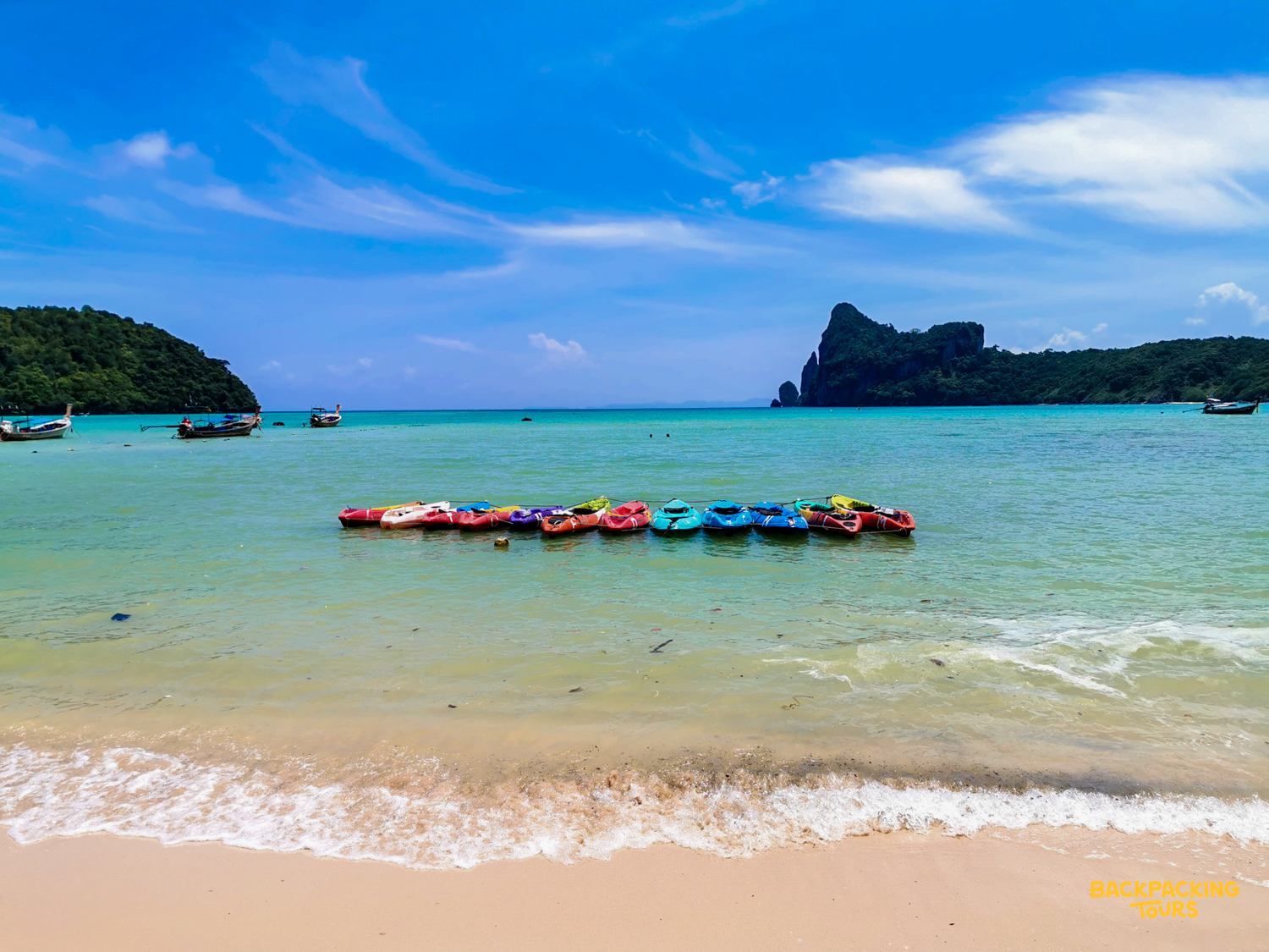Colorful kayaks line the turquoise waters of a sandy beach in Thailand's stunning Phi Phi Islands.