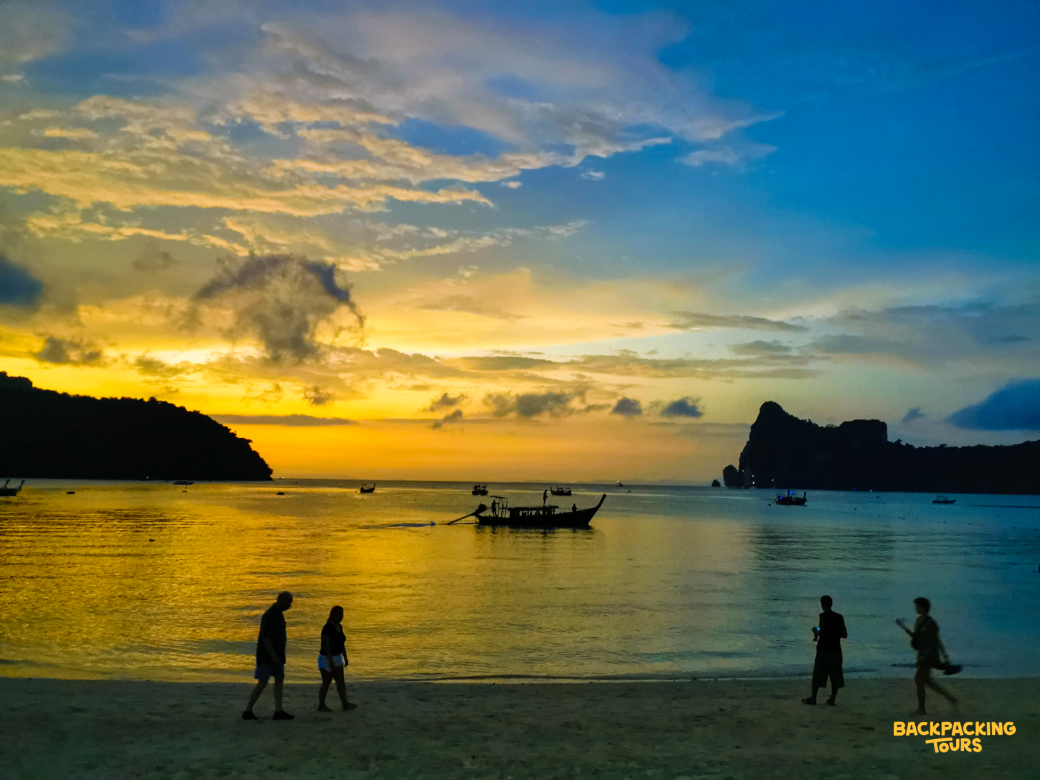 Silhouetted people stroll along the sandy beach at sunset in Thailand's stunning Phi Phi Islands.
