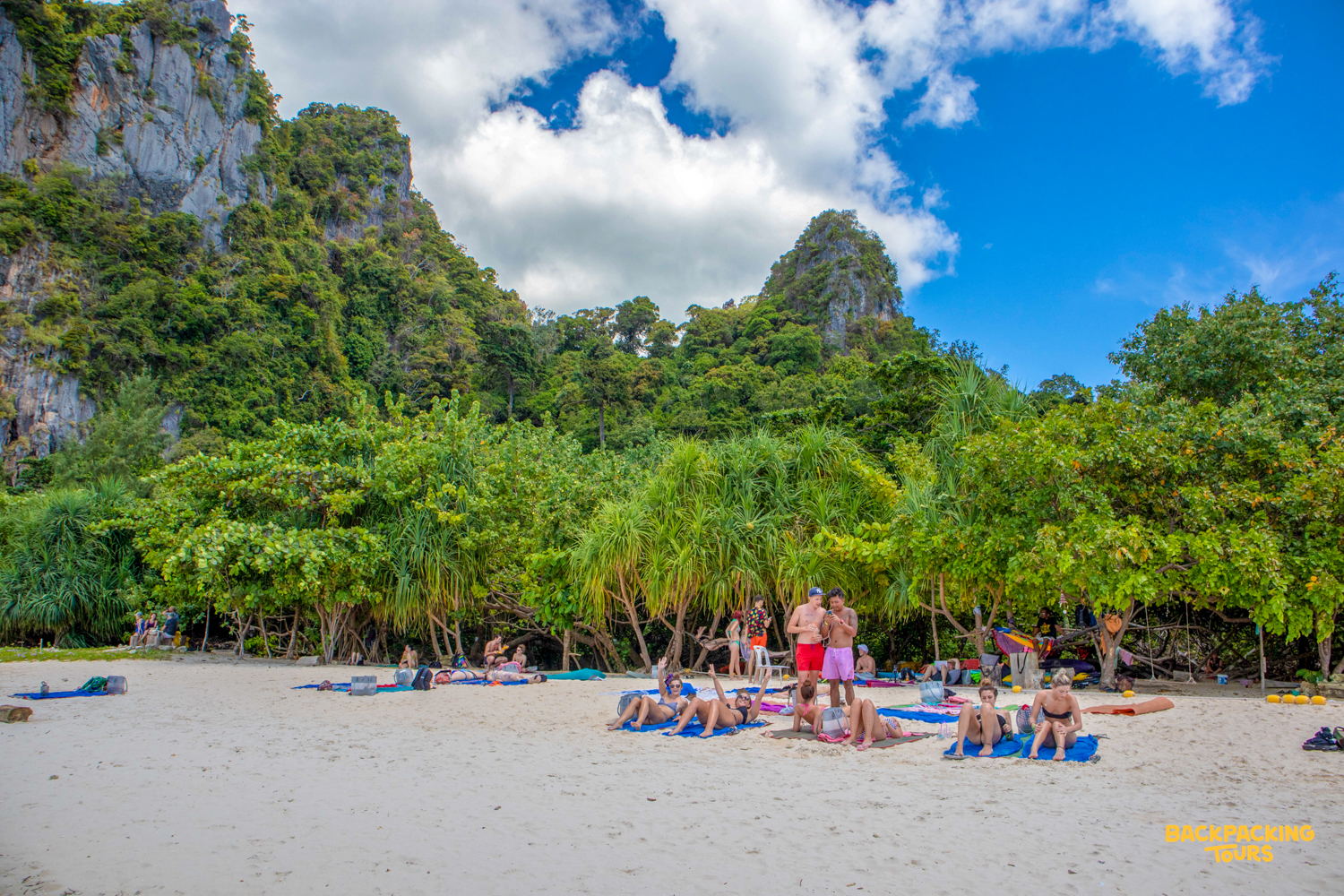 Tourists relax on a white sand beach in Krabi, Thailand, framed by lush green cliffs.