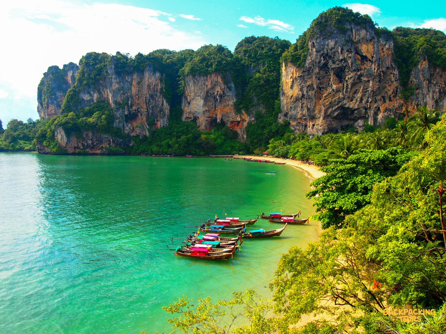 Traditional longtail boats rest on clear turquoise water in a beautiful Krabi bay, framed by limestone cliffs.