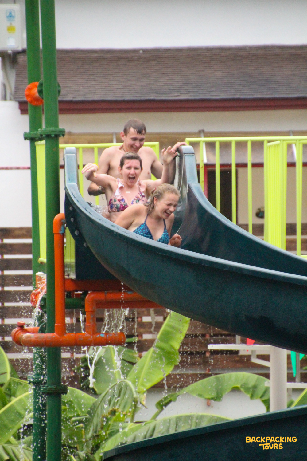 Three happy travelers enjoying a thrilling ride down a water slide, splashing water everywhere.