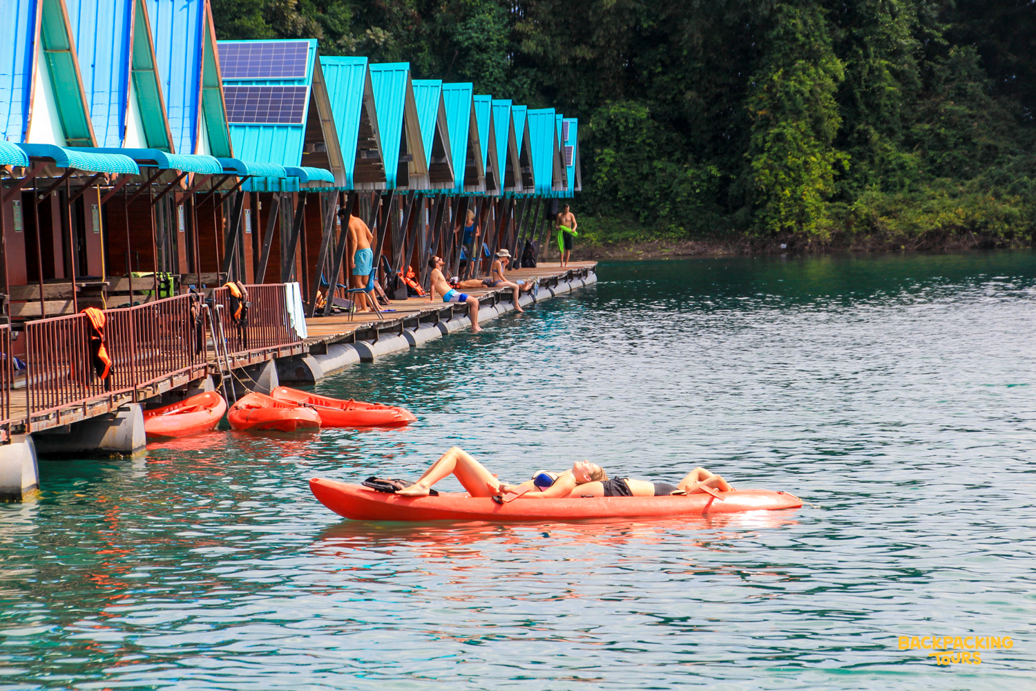 A person relaxes on a kayak in the clear waters near floating bungalows at Khao Sok National Park.