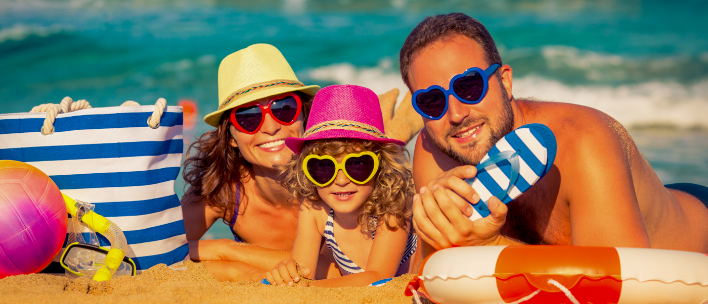 A happy family wearing hats and heart-shaped sunglasses relaxing on a sandy beach in Phuket.