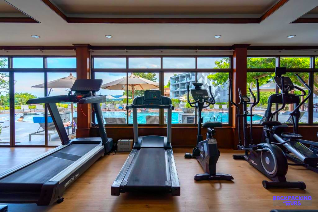 A modern hotel gym with various fitness machines and a refreshing view of the outdoor pool in Phuket.