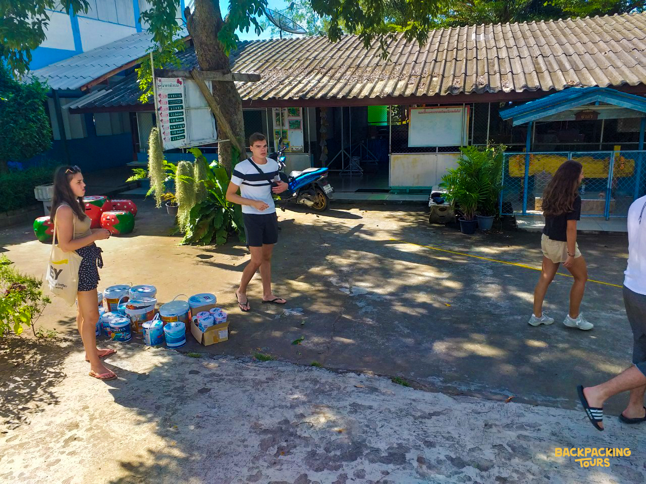 Volunteers gather in a sunny outdoor area, preparing for activities in a Thai community.