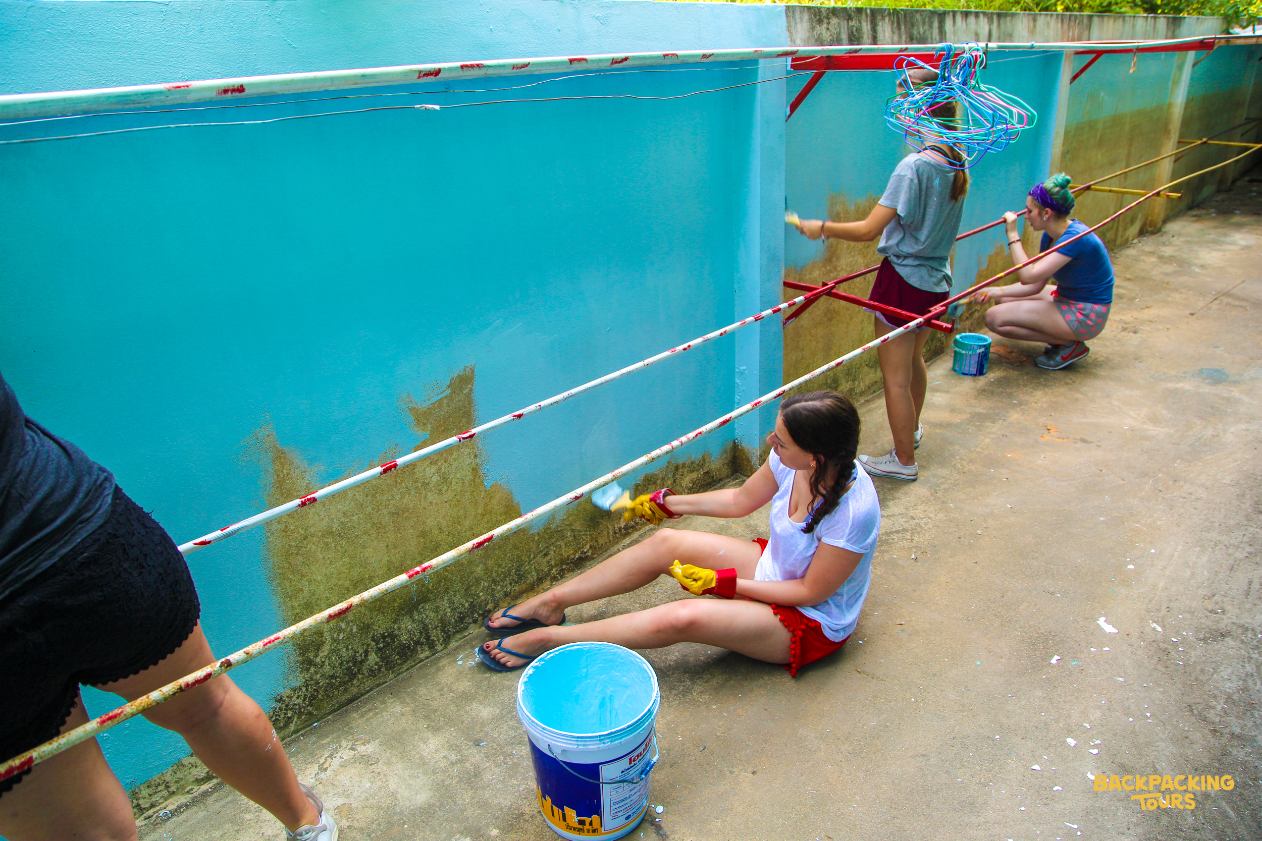 Three volunteers paint a light blue wall, transforming an outdoor area with bright colors.