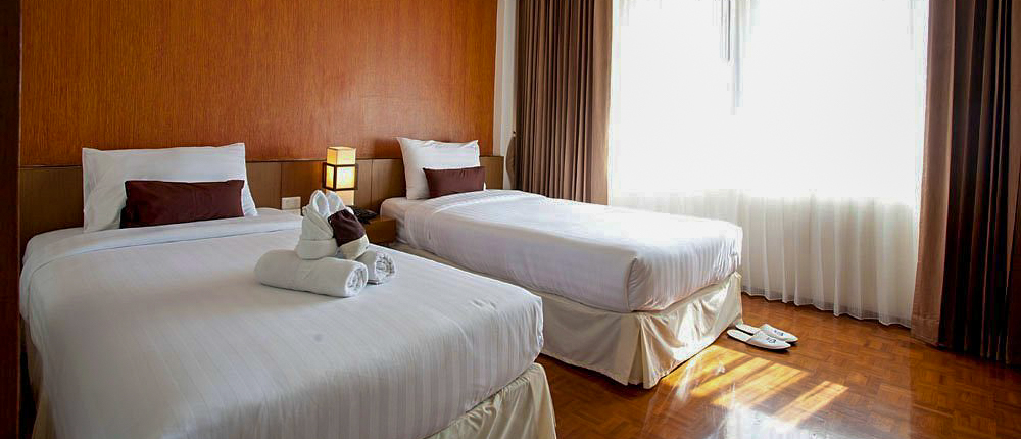 Comfortable hotel room in Chiang Mai with two twin beds, decorative towels, and a bright window.