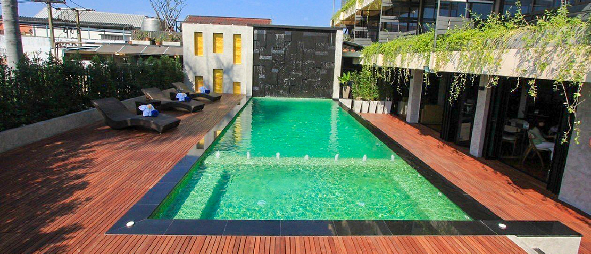 A modern hotel swimming pool with green water and wooden deck, perfect for relaxing in Chiang Mai.