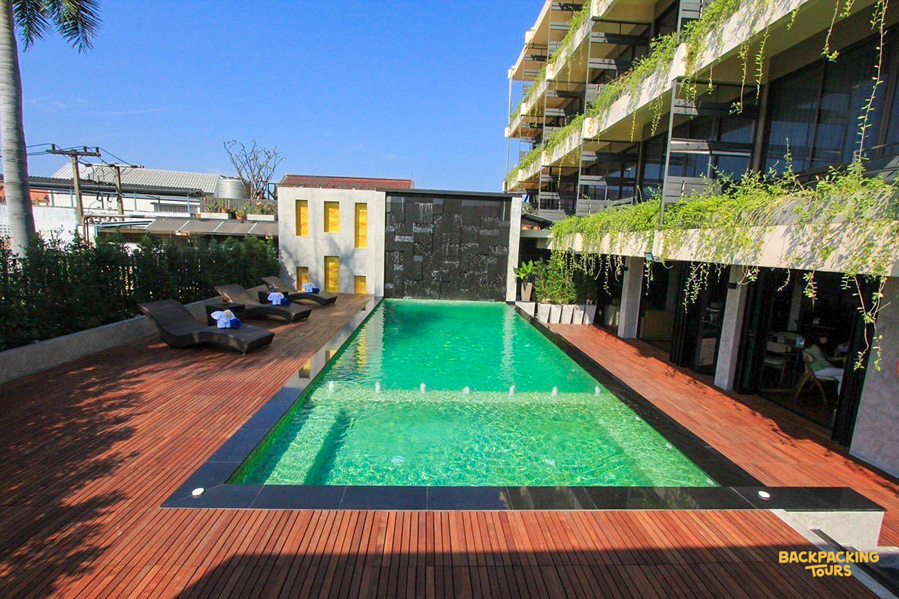 A refreshing green swimming pool with a wooden deck and modern hotel building in sunny Chiang Mai.