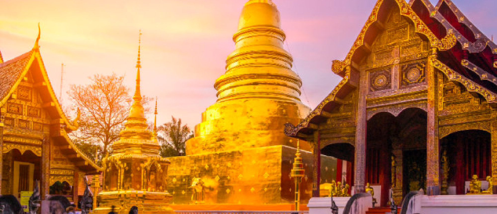 Golden spires and ornate temple buildings glow under a vibrant sunset at Doi Suthep in Chiang Mai.