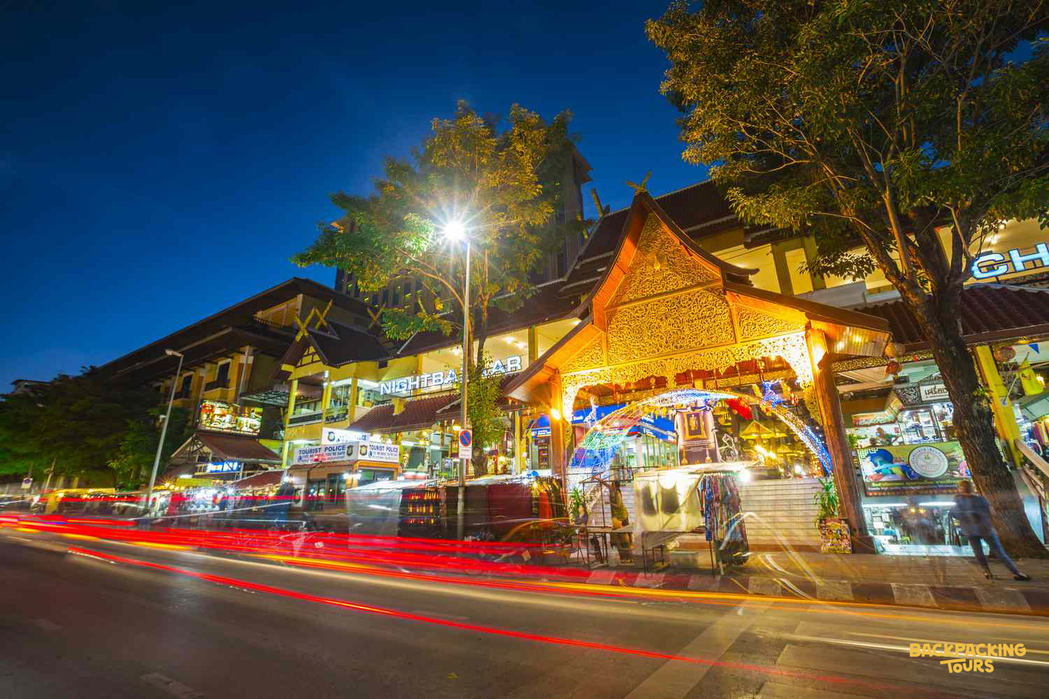 A vibrant night scene in Chiang Mai, with traditional Thai architecture and streaks of vehicle lights.