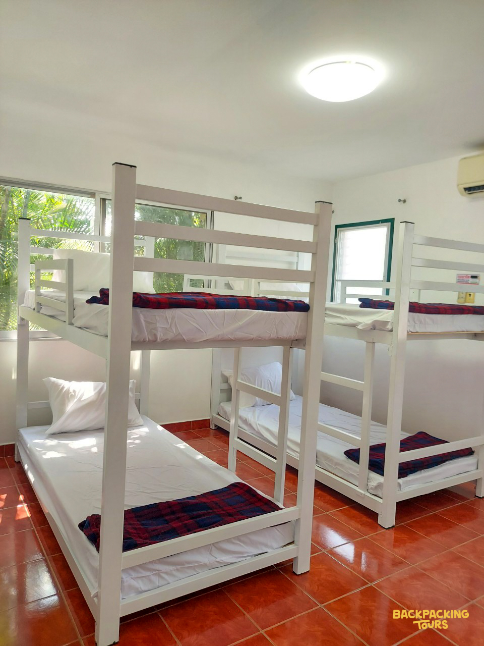 Bright volunteer accommodation room with white bunk beds, clean linens, and a warm tiled floor.