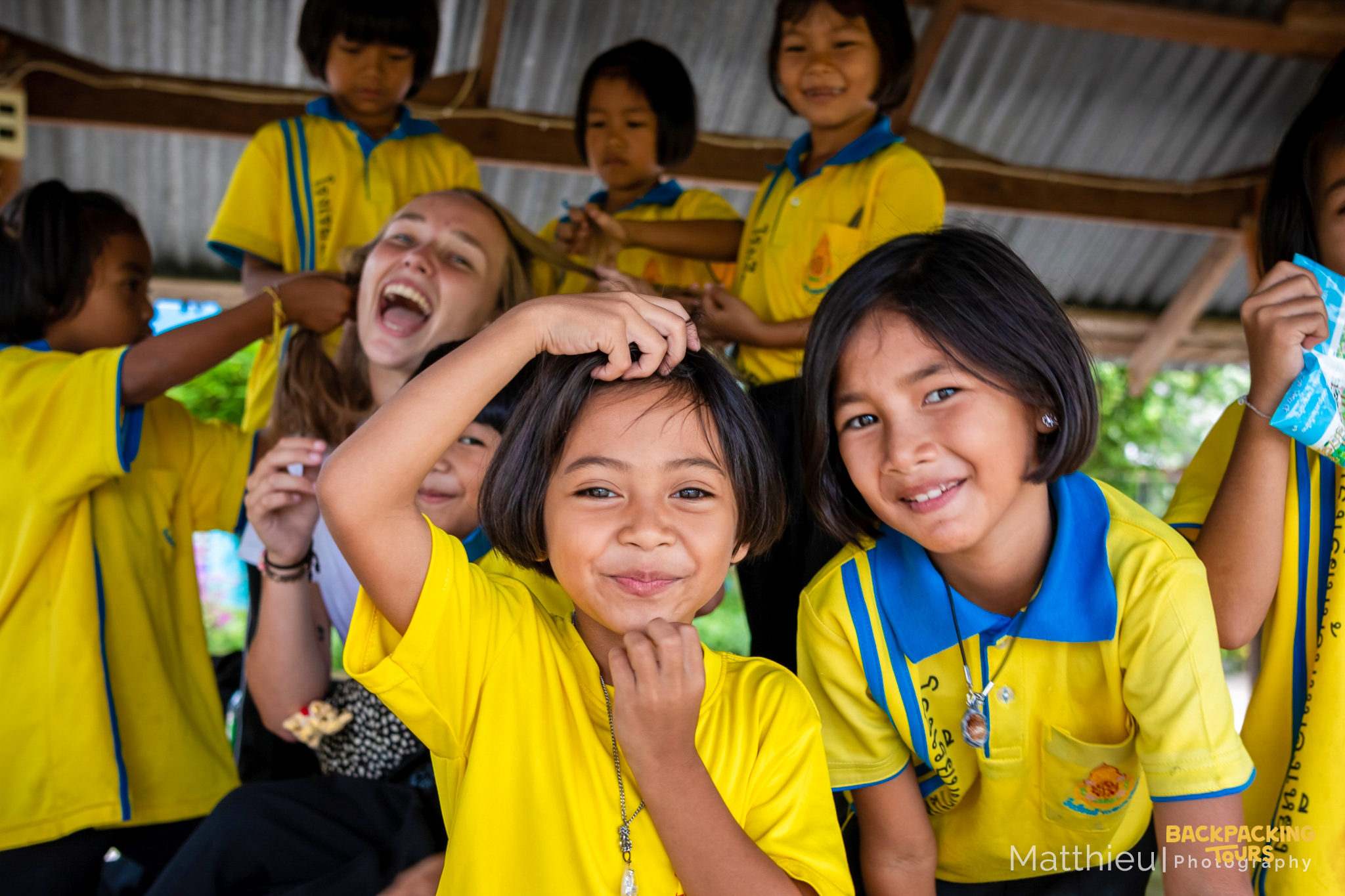 Happy Thai kindergarten children in yellow uniforms play with a laughing volunteer.